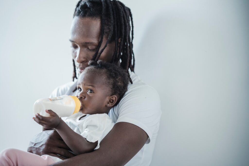 african american father holding daughter drinking a baby bottle of milk