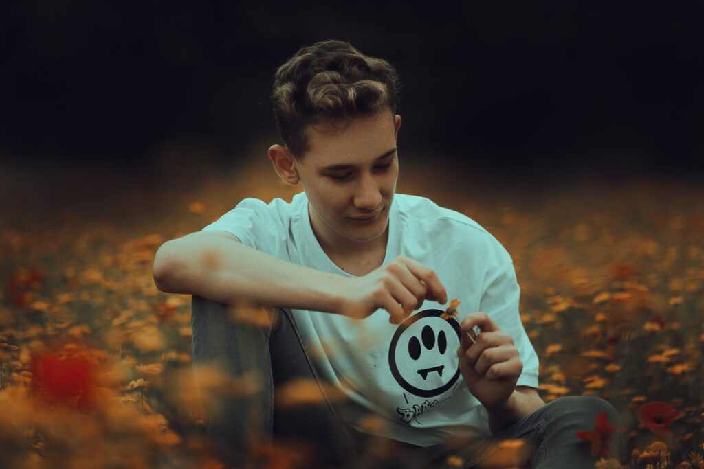 young teenage boy playing with a daisy in a field